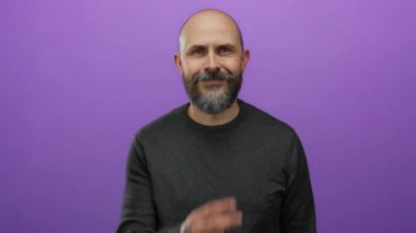 Mor arka planda sakallı kel bir adam. El işaretleri ve dövmesi ile ihtiyatlı olduğunu söylüyor..