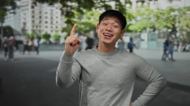 Genç bir adam hareketli bir şehir caddesinde güvenli bir şekilde el kol hareketi yaparken açık havada, bulanık şehir geçmişiyle neşeli bir fikir dile getiriyor ve insanlar olay yerinden geçiyor..