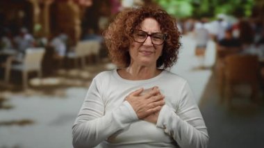 Dışarıdaki teras restoranında ifade veren bir kadın. Bulanık insanlar ve arka planda gözlük takan ve günlük kıyafetlerle duygularını ifade eden masalarla.