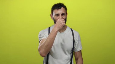 Sakallı İspanyol bir adam, beyaz gömlek ve pantolon askısı giymiş, özel hayat kavramı taşıyan parlak sarı arka plana karşı gizli bir jest yapıyor..