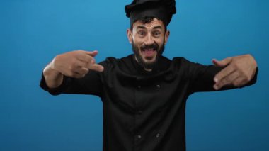 Şef coşkuyla kendini gösteriyor, parlak mavi bir arka plana karşı siyah bir üniforma giyiyor, aşçılık uzmanlığına karşı gurur ve güven gösteriyor..