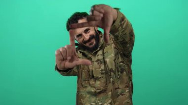 Askeri üniformalı İspanyol bir adam yeşil arka planda poz veriyor ve elleriyle bir çerçeve oluşturuyor..