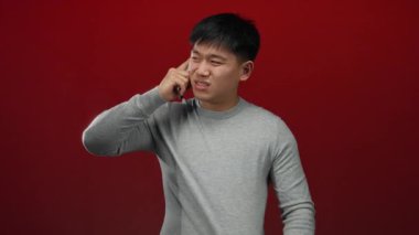 Kırmızı arkaplan önünde telefonla konuşan genç adam görünür bir merak ve etkileşimle duygusal bir bağlantı kuruyor..