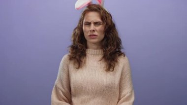 Kıvırcık saçlı, tavşan kulaklı bir kadın, izole edilmiş mor bir arka plana karşı şaşkın, rahat bir kazak giymiş, tuhaf bir tatil belirsizliğini yakalıyor..