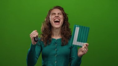 Araba anahtarlarını tutan kadın ve öğrenci tabelası, izole edilmiş yeşil arka plana sevinç ve heyecanla bakıyor.