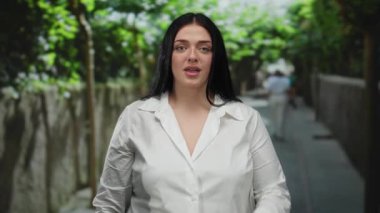 Bir kadın şehir caddesinde dışarıda dikilirken sessiz hareketler yapıyor, sakin ve huzurlu bir atmosferi somutlaştırıyor gün ışığında kentsel çevrede..