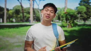 Açık hava parkında gülümseyen kitaplarla genç bir adam..