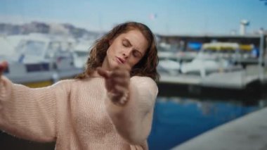 Sahildeki bir marinada rahat bir kazakla duygularını ifade eden bir kadın. Arka planda tekneler var..