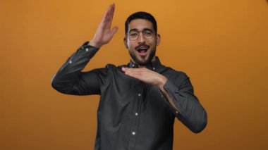 Genç İspanyol adam, canlı turuncu bir arkaplan karşısında coşkuyla el hareketi yapıyor, yaratıcılığını ve ifadesini gösteriyor..
