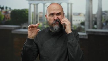 Cep telefonuyla Roma harabelerine karşı konuşan sakallı kel bir adam, endişeli görünüyor ve tarihi mekanda el kol hareketi yapıyor..