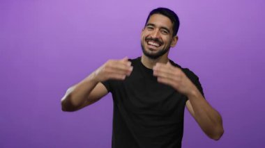 Genç adam, portre tarzında mor arka planda elleri ile gülüyor, neşeli ve neşeli duygular yayıyor.