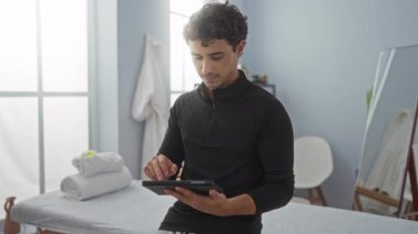 Genç adam spa odasında havlu ve sandalyeli tablet kullanıyor. Parlak sağlık merkezinde görülebiliyor.