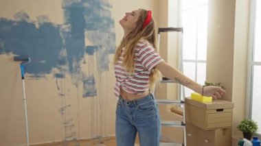 Yeni boyanmış bir oturma odasında içi boş merdivenler ve kutularla gülümseyen kadın, ev yenileme ve yeni bir başlangıç zevkini yansıtıyor..