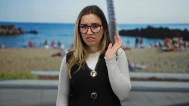 Genç bir kadın sahilde palmiye ağaçları ve okyanus zeminiyle saygısızca jest yapıyor. Güneşli bir deniz manzarasında reddedildiğini ya da hoşnutsuzluğunu dile getiriyor..