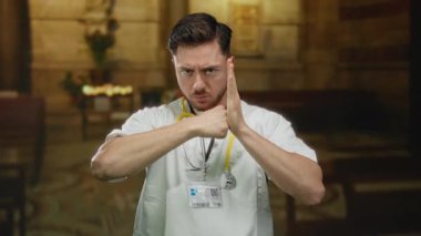 Sert ifadeli bir doktor, loş bir kilise ortamında boynuna steteskop takarak kavga eder..