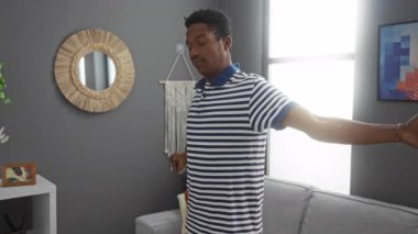 Gri duvarları, dekoratif aynası ve parlak pencere ışığı olan modern oturma odasında uzanan çizgili gömlekli genç adam..