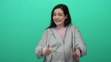 Yeşil arka planda mutlu bir şekilde gülümseyen, gri kapüşonlu, baş parmak gösteren, onay ya da başarı gösteren bir kadın..