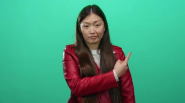 Kırmızı ceketli kadın yeşil arka planı işaret ediyor. Duygularını gösteriyor. Düşünceli, şık, çekici bir kadın..
