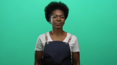 Önlük takan kadın parlak yeşil arka plana karşı duruyor kendine güven ve duruş yayıyor..