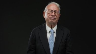 İş elbisesi giymiş kıdemli bir adam, izole edilmiş siyah arka plana karşı kulaklarını kapatır, gözleri kapalı rahatsızlık ve hayal kırıklığını ifade eder, güçlü bir insani duyguyu gösterir..