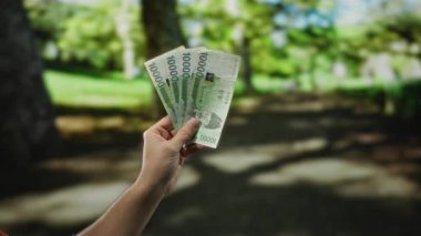 Güney Kore 'yi elinde tutan bir adamın eli parkın açık havada, bulanık yeşil bahçeli arka planında para, finans, ekonomi ve açık hava yaşam tarzını sembolize eden banknotlar kazandı..