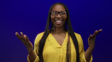 Canlı mavi bir duvarın önünde güvenle gülümseyen, sarı bir gömlek ve gözlük takan, mutluluk ve gururu somutlaştıran bir kadın..