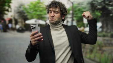 Açık havada akıllı telefonla başarıyı kutlayan balıkçı yaka ve takım elbise giyen şehir caddesinde gündüz vakti yumrukla zafer ilan eden bir adam..