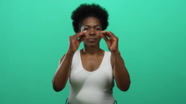 İzole edilmiş yeşil bir arkaplanda jestler yapan kadın, hareket yoluyla ifade ve duygu gösterir, bireyselliği ve kültürü vurgulayan canlı bir fotoğrafta yakalanır..