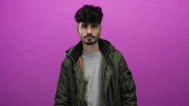 Yeşil ceketli genç İspanyol adam, tetikte olduğunu ve dikkat ve dikkat gösterdiğini belirten pembe bir arka planda parmağı ile ihtiyatlı bir jest yapıyor..