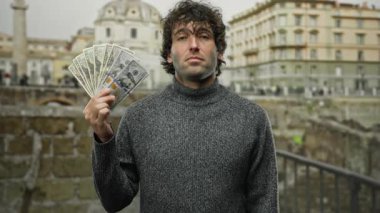 Bir şehir caddesinde Amerikan doları banknotları tutan, şehir mimarisi arasında zenginlik ve güven gösteren, açık şehir yaşam tarzını ön plana çıkaran bir adam..