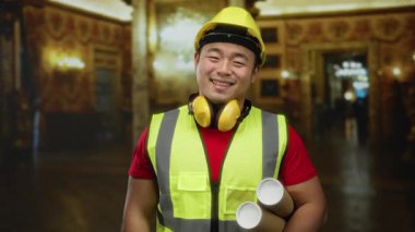 Kasket ve güvenlik yeleği giyen genç bir adam, bir müze ortamının planlarını tutuyor, mimari ve kültürün bir karışımını içeriden gülümseyerek gösteriyor..