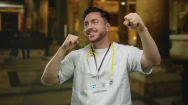 Genç bir adam, sakallı ve steteskoplu gülümseyen bir doktor, kilisenin içinde duruyor, kendine güvenen jestleri olan beyaz bir ceket giyiyor, umudu ve iyileşmeyi simgeliyor..