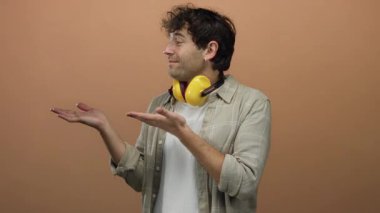 Ses geçirmez kulaklık takan İspanyol adam turuncu arka planda el ele tutuşuyor, neşeli ve rahat görünüyor..