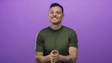 Genç adam mor bir duvara karşı jestler yapıyor, duygularını dışa vuruyor ve özgüvenli bir gülümseme ve günlük bir stil ile etkileşime giriyor..