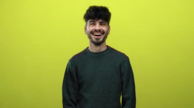 Parlak sarı arka planda gülümseyen genç adam, günlük süveter giyiyor. Parlak ve neşeli bir portre pozuyla mutluluk ve kendine güveni ifade ediyor.