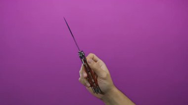 Bıçağın dizaynını ve renk kontrastını gözler önüne seren canlı pembe bir arka planda bir sustalı bıçak tutan adamın eli..