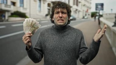 İspanyol adam şehir caddesinde hayal kırıklığına uğramış bir şekilde Rus rublesi tutuyor..