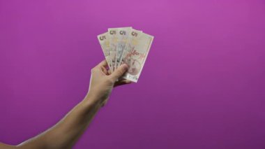 Canlı mor bir zemin üzerinde Türk lira banknotları tutan adam, münferit detaylar ve el hareketi öne çıkan para ve finans temaları ile para sergileniyor.