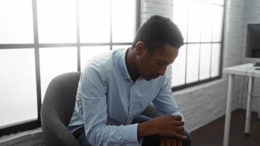 Ofisteki genç adam, büyük pencereli modern iş ortamında düşünceli bir şekilde iç çamaşırlarıyla düşünceli bir şekilde oturuyor.