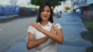 Canlı bir şehir caddesinde güven içinde gülümseyen bir kadın, kolları çapraz, renkli bir duvar ve parlak bir gün ışığı, açık havada beyaz bir gömlek giyerek.