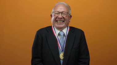 Takım elbiseli kıdemli adam turuncu arka plana karşı altın madalyayla gülümsüyor, iş ortamındaki başarıyı ve başarıyı simgeliyor..