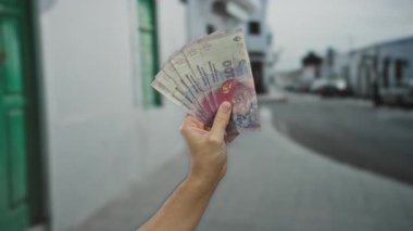 Bir şehir caddesinde elinde Arjantin pezosu olan bir adam açık bir şehir zeminine karşı banknotlar sergiliyor. Finansal işlemlerin özünü yakalıyor..