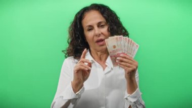 Elinde Kolombiya pezosu olan gülümseyen bir kadın izole edilmiş yeşil arka planda kameraya bakıyor..