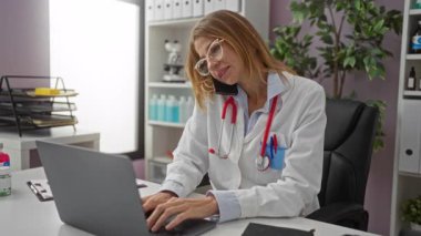 Klinikte telefonla konuşan, gözlük ve steteskop takan, tıbbi ekipman ve evrak işleriyle çevrili bir kadın doktor..