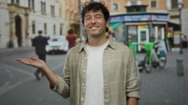 Açık havada güneşli bir günde insanların, motosikletlerin ve binaların bulanık geçmişleriyle dolu canlı bir şehir sokağında gülümseyen ve elini uzatan İspanyol bir adam..