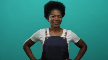 Önlüklü kendinden emin Afrikalı Amerikalı kadın izole edilmiş yeşil arka plana karşı elleri kalçasında gülümseyen.