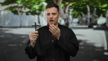 Şehir caddesinde karşıdan karşıya geçen adam siyah dini giysiler giymiş canlı yeşil doğa ve kentsel altyapının arasında umut ve inanç ifadesiyle yukarı bakıyor..