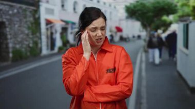 Turuncu hapishane tulumu giyen kadın sokakta dikiliyor hayal kırıklığına uğramış ve kafası karışmış bir halde..