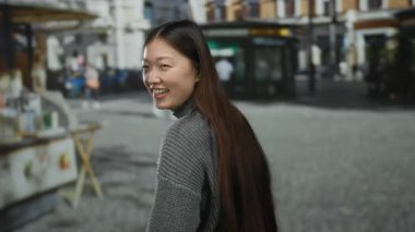 Gülümseyen bir kadın, Çin 'de bir şehir caddesinde gri bir kazak giyip uzun saçlarını gösterirken başparmağını kaldırıyor..