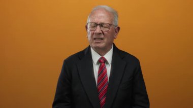 Takım elbiseli yaşlı işadamı canlı turuncu arka plana karşı göğüs ağrısı gösteriyor. Tecrit ortamında klasik yaşlı sağlık stresi gösteriyor..